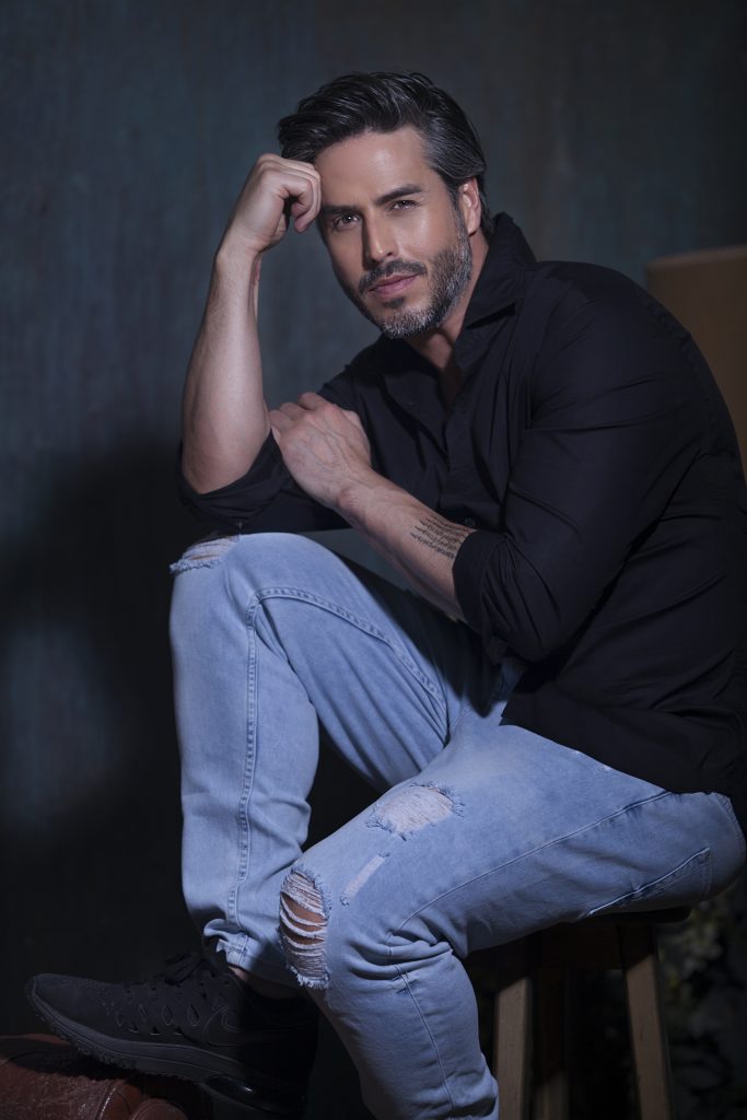 Hombre guapo sentado en una silla sonriendo Raúl Olivo, actor y portada de la segunda edición de la revista impresa y digital, Revista Bfit